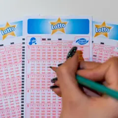 Ręka z ołówkiem zaznacza liczby na kuponach Lotto. Poznaj, jakimi metodami można zawierać zakłady gier liczbowych, wybierając swoje szczęśliwe cyfry.