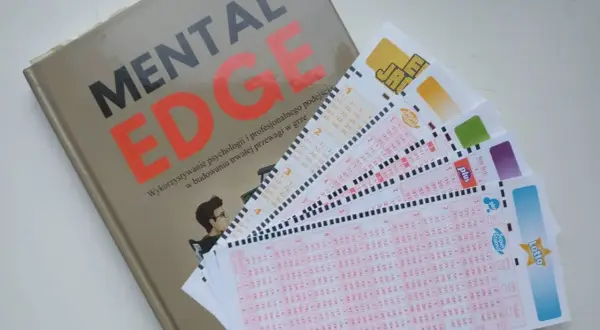 Książka "Mental Edge" i kilka kuponów Lotto ułożonych na białym tle.