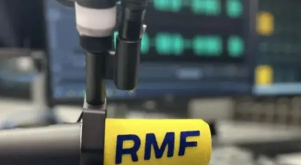Mikrofon radiowy z logo RMF FM na tle ekranu z falami dźwiękowymi.