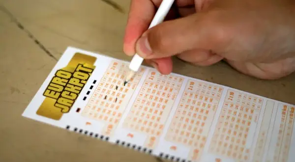 Dłoń z ołówkiem zaznacza liczby na kuponie Eurojackpot.